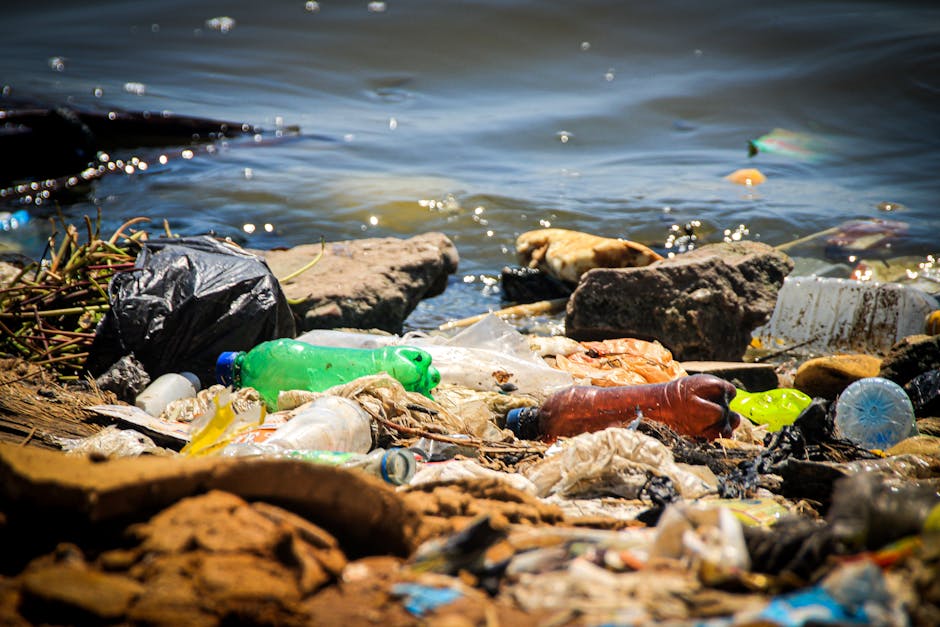 A large landfill site filled with a substantial accumulation of mixed waste materials, including plastics, textiles, and household refuse, with multiple yellow excavators actively engaged in loading a