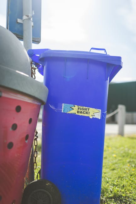 A close-up view of a white woven polypropylene sack filled with garden waste, including small branches, green leaves, and broken debris. A person's hand, wearing a white glove, is holding the bag open
