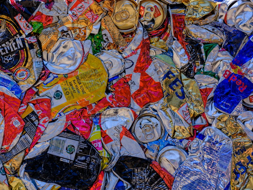 Two large black plastic rubbish bags, slightly crumpled and tied at the top, are positioned on a paved sidewalk next to a curb. The bags are filled with waste, with visible creases and a shiny finish